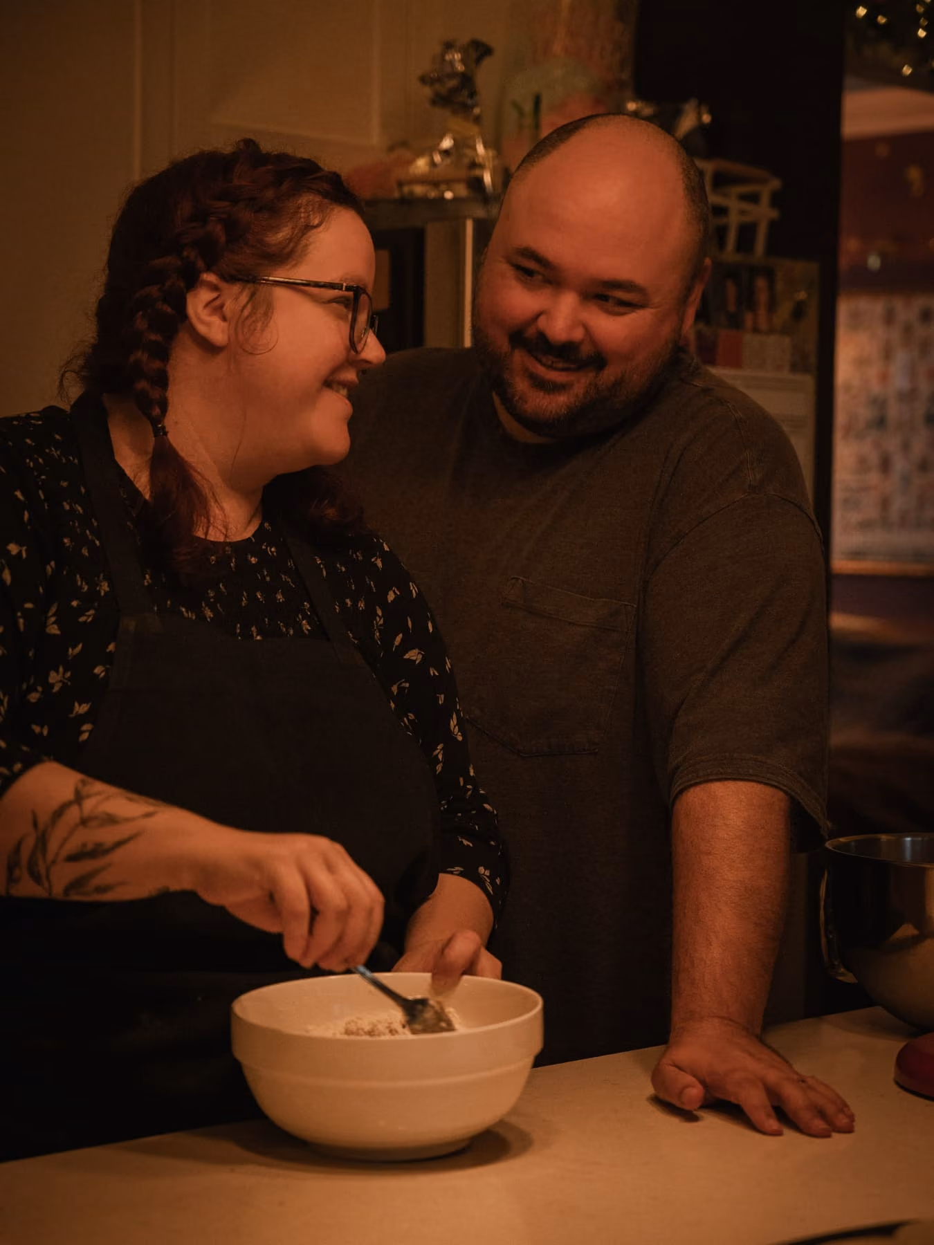 The couple laugh together over a mixing bowl.
