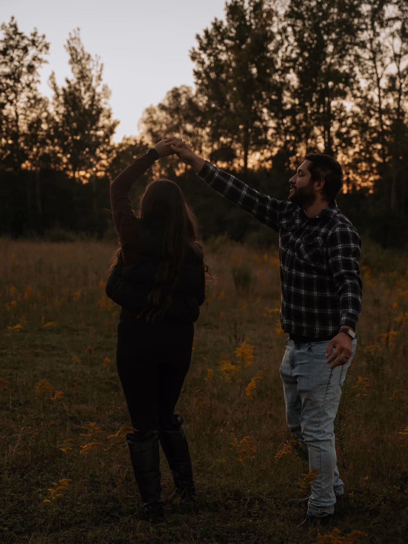 A couple dance in a field at dusk, trees dark behind them.